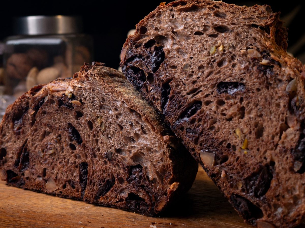 Angeschnittenes Schoko-Sauerteigbrot mit Schokostückchen und Nüssen in einer dunklen Umgebung.