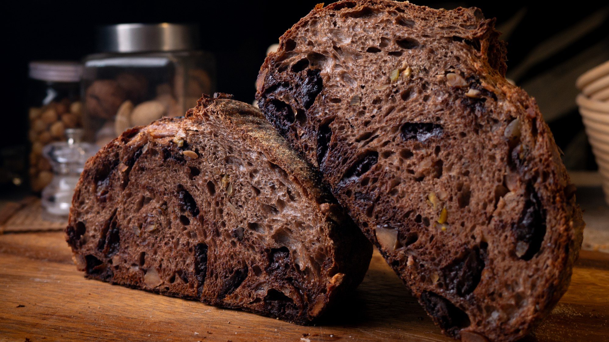 Angeschnittenes Schoko-Sauerteigbrot mit Schokostückchen und Nüssen in einer dunklen Umgebung.