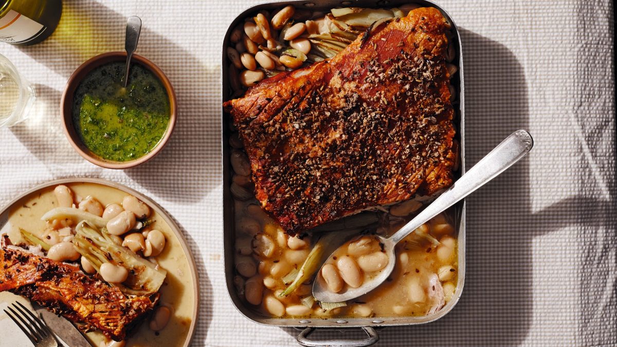 Eine Auflaufform mit dem Schweinebauch und daneben eine kleine grüne Schale mit dem Dip. Alles im Sonnenlicht direkt von oben fotografiert auf heller Tischdecke.