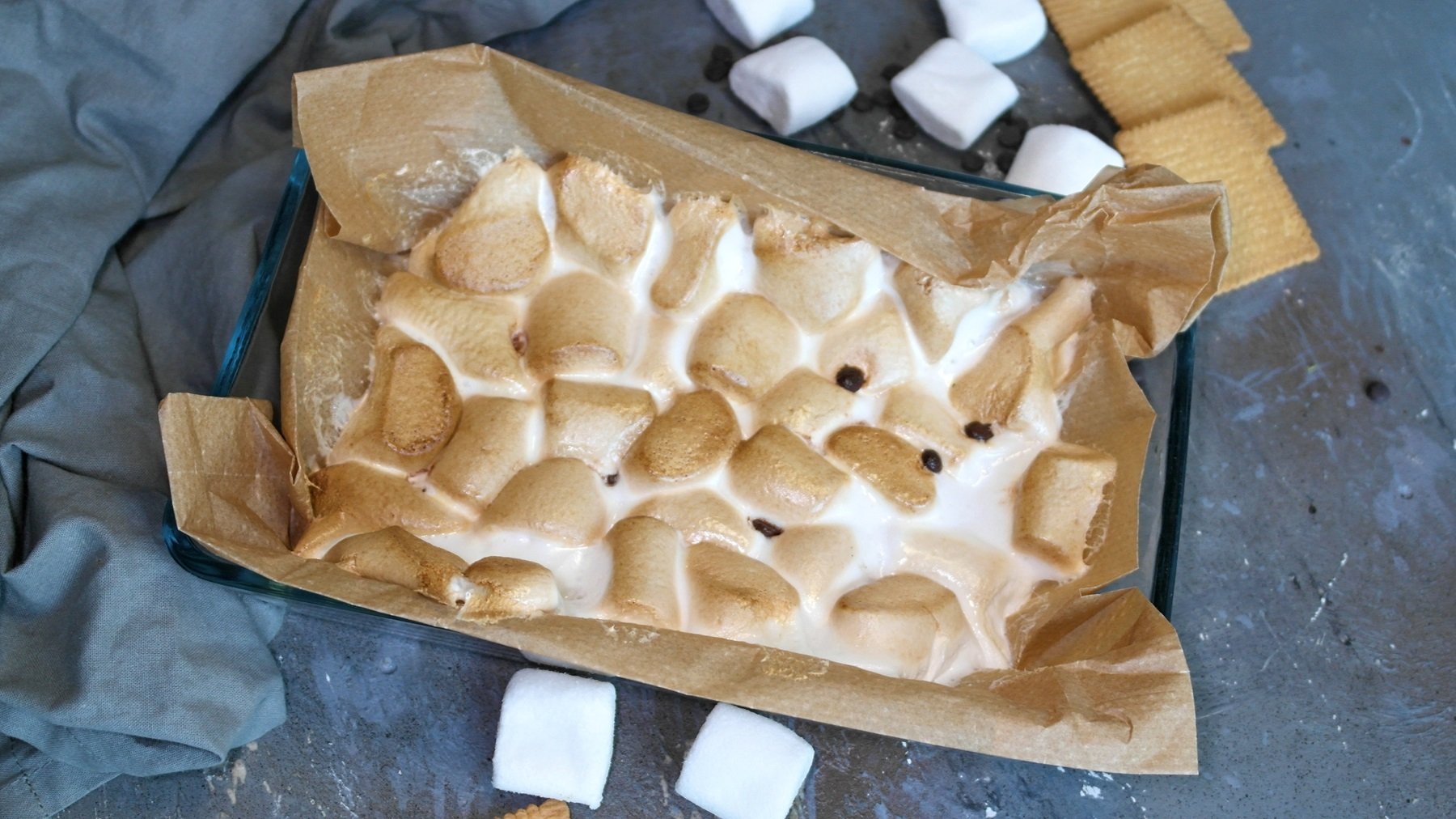 Eine Auflaufform aus Glas mit den karamellisierten Marshmallows. Alles auf steinernem Untergrund von oben fotografiert.