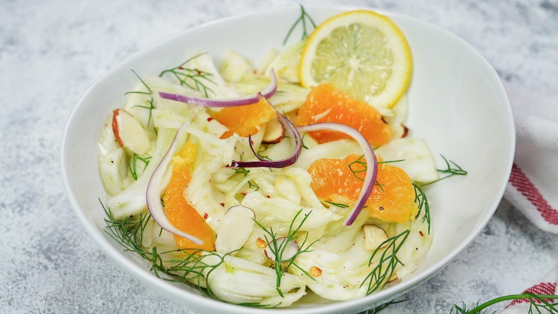 Eine weiße Schüssel mit dem arabischen Fenchel-Orangen-Salat auf grauem Untergrund von schräg oben fotografiert.