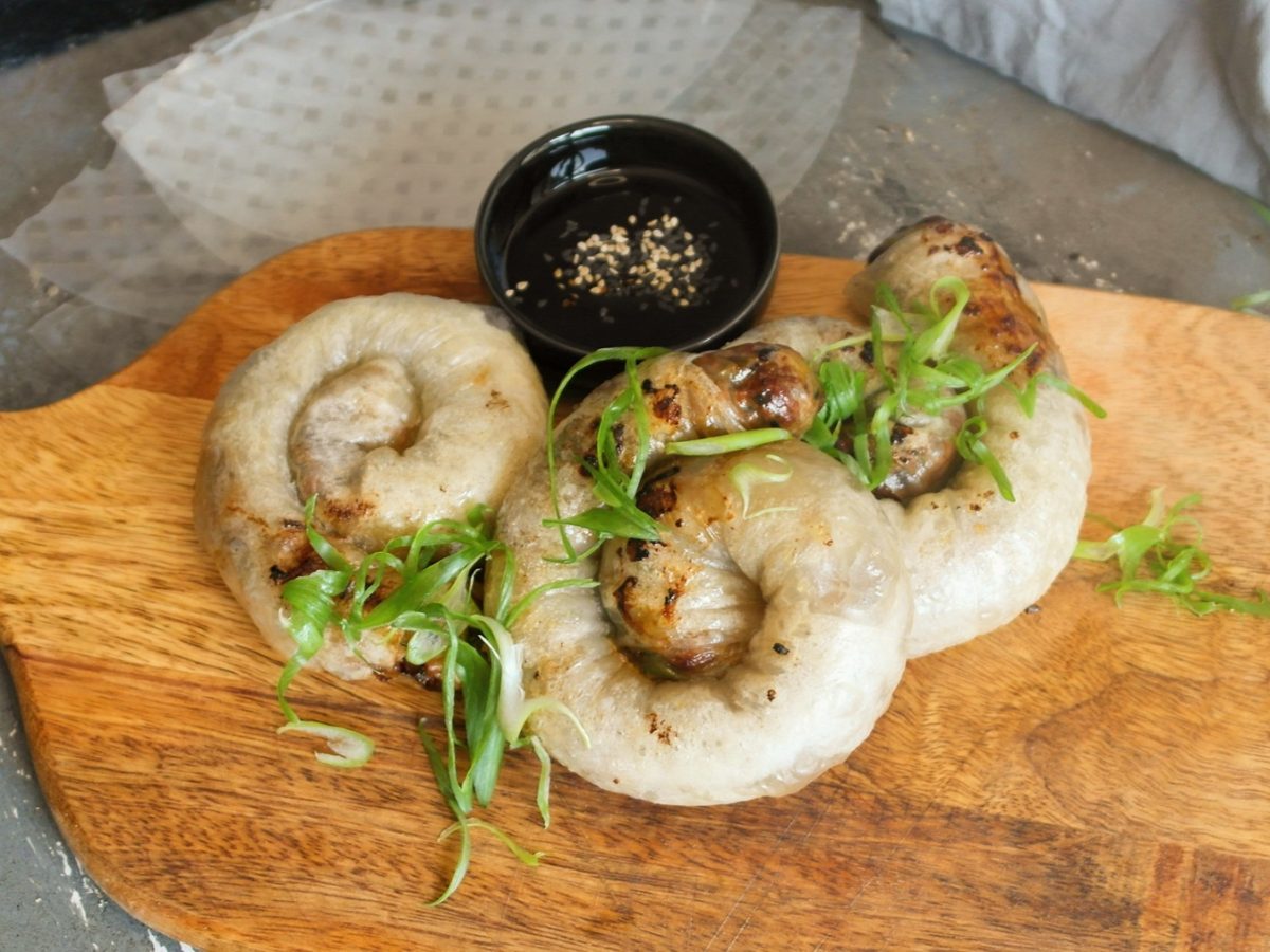 Die knusprigen Teigschnecken auf einem Holzbrett mit Teriyakisauce und Sesam. Alles von schräg oben fotografiert.