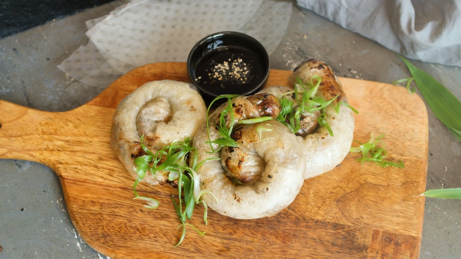 Die knusprigen Teigschnecken auf einem Holzbrett mit Teriyakisauce und Sesam. Alles von schräg oben fotografiert.