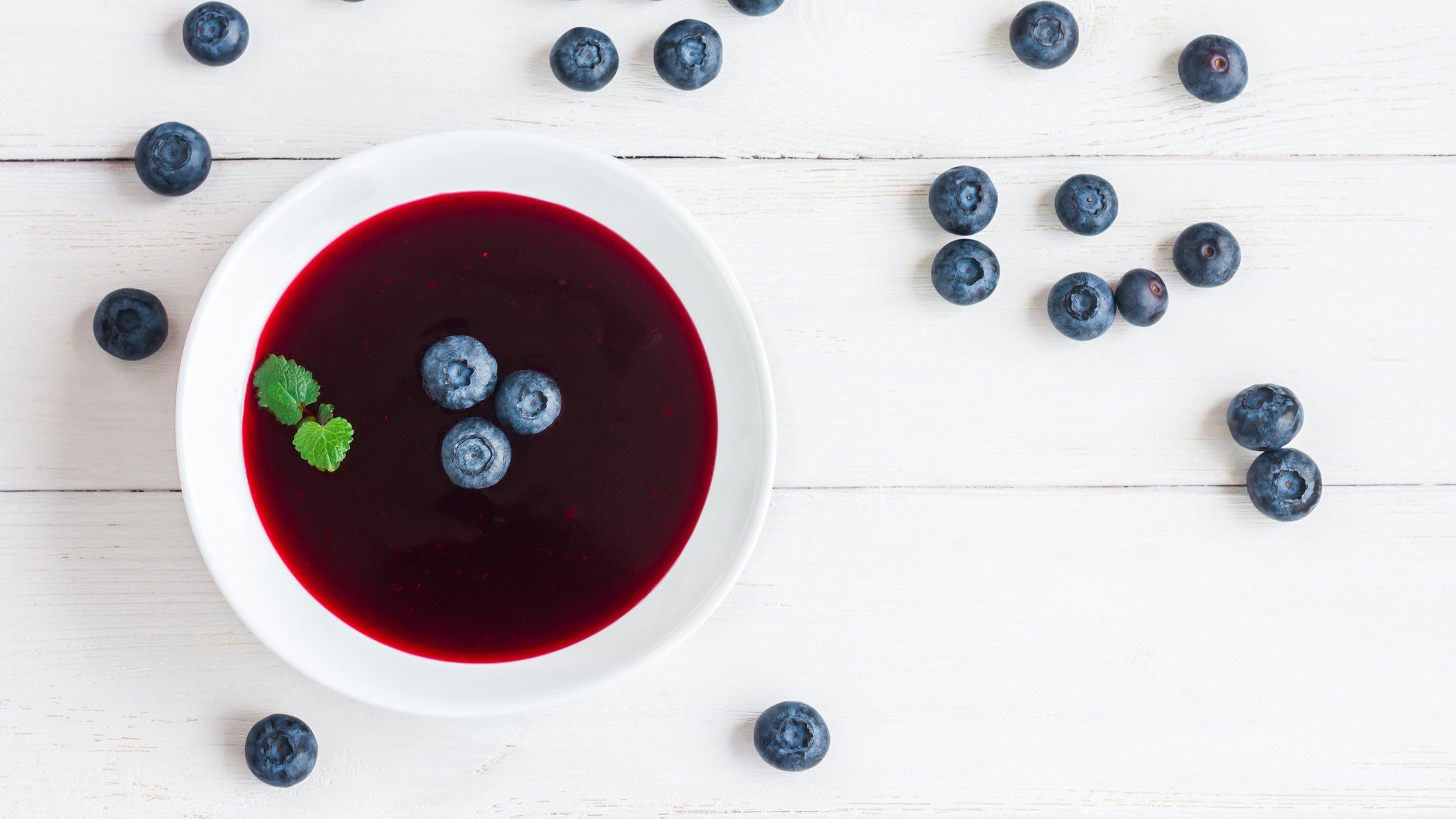 Sommerliche Blaubeersuppe mit Blaubeeren und Minze, stilvoll angerichtet auf hell gebeiztem Holzhintergrund.