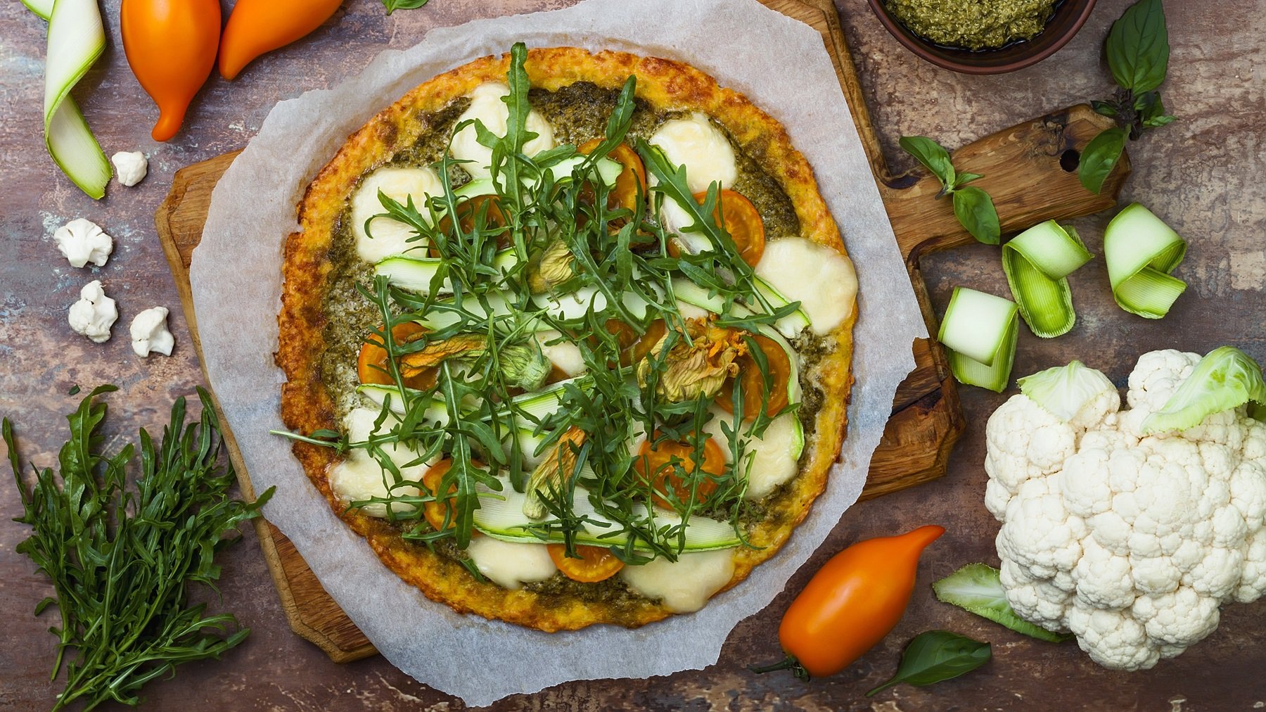 Die Pizza auf einem dunklen Tisch mit den passenden Zutaten daneben direkt von oben fotografiert.