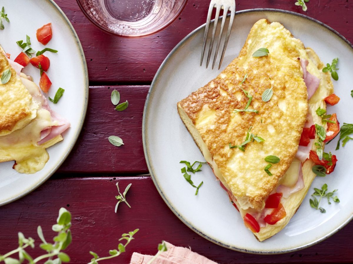 Zwei Portionen Cordon-bleu-Omelett auf weißen Tellern vor rotem Hintergrund, darauf Oregano verteilt.