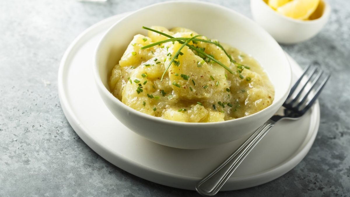 Bayrischer Kartoffelsalat in rundem, hellen Teller. / Holzboden / Frontal