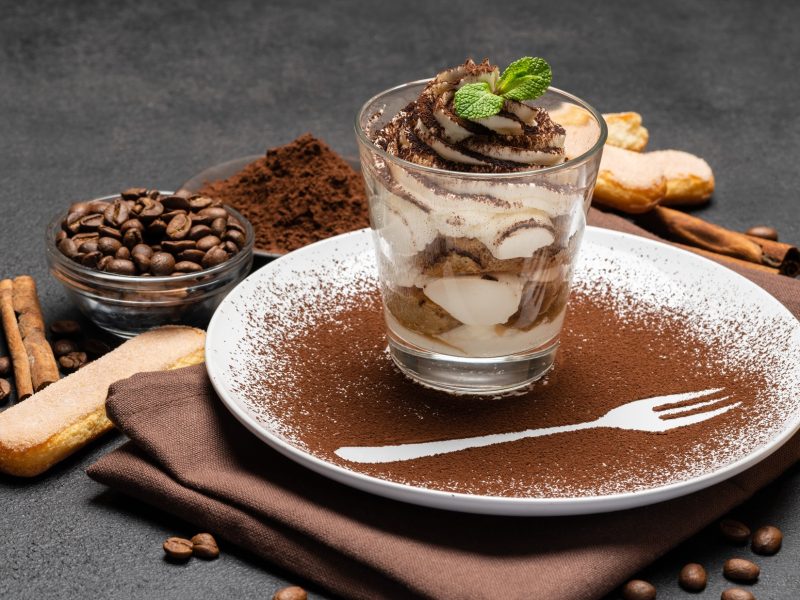 Espresso-Tiramisu im Glas / Untergrund runder Teller, bestäubt mit Kakaopulver / Frontal