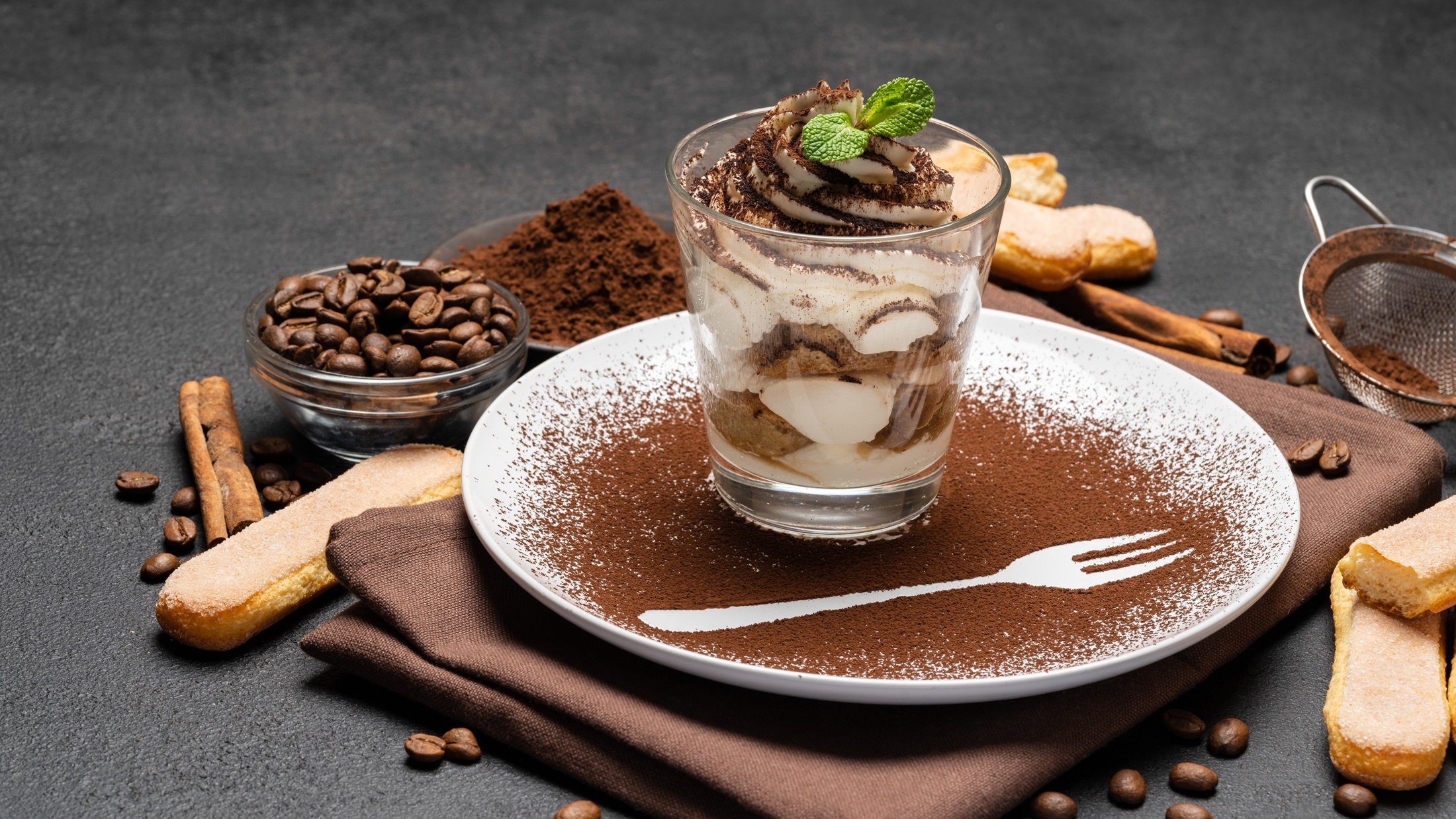 Espresso-Tiramisu im Glas / Untergrund runder Teller, bestäubt mit Kakaopulver / Frontal