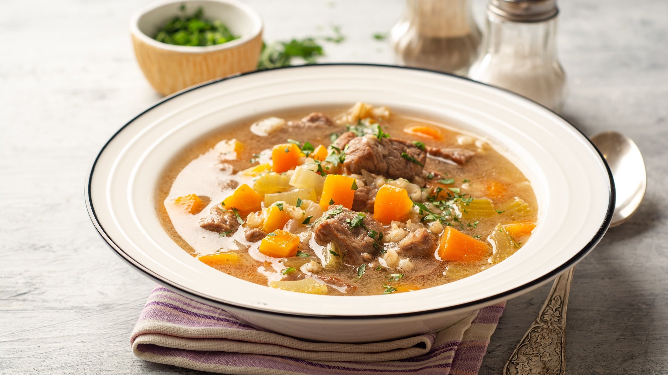 Rindfleischsuppe in einem hellen, runden Teller / Untergrund Holz