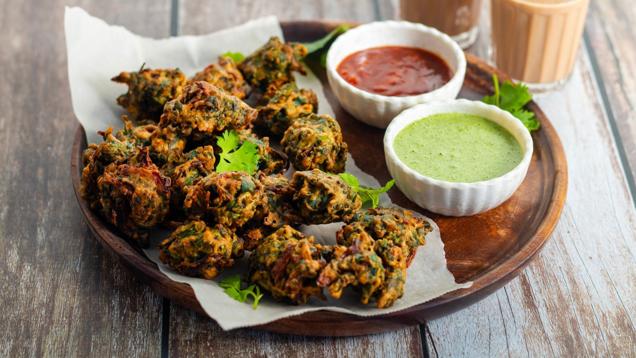 Spinat-Pakoras und zwei Schalen mit Saucen auf einem runden Tablett- / Untergrund rustikales Holt / Draufsicht schräg