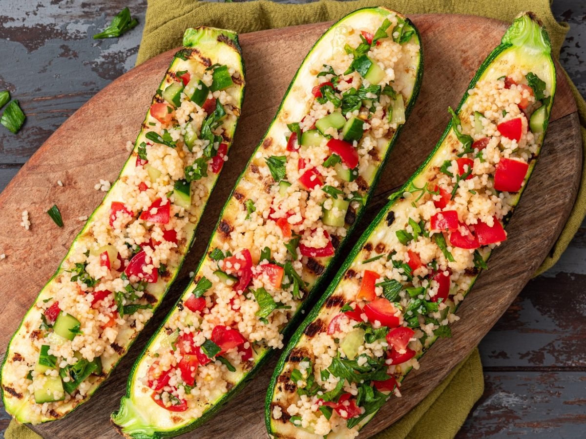 Drei gefüllte Zucchinihälften mit dem Couscous auf einem grauen Untergrund direkt von oben fotografiert.