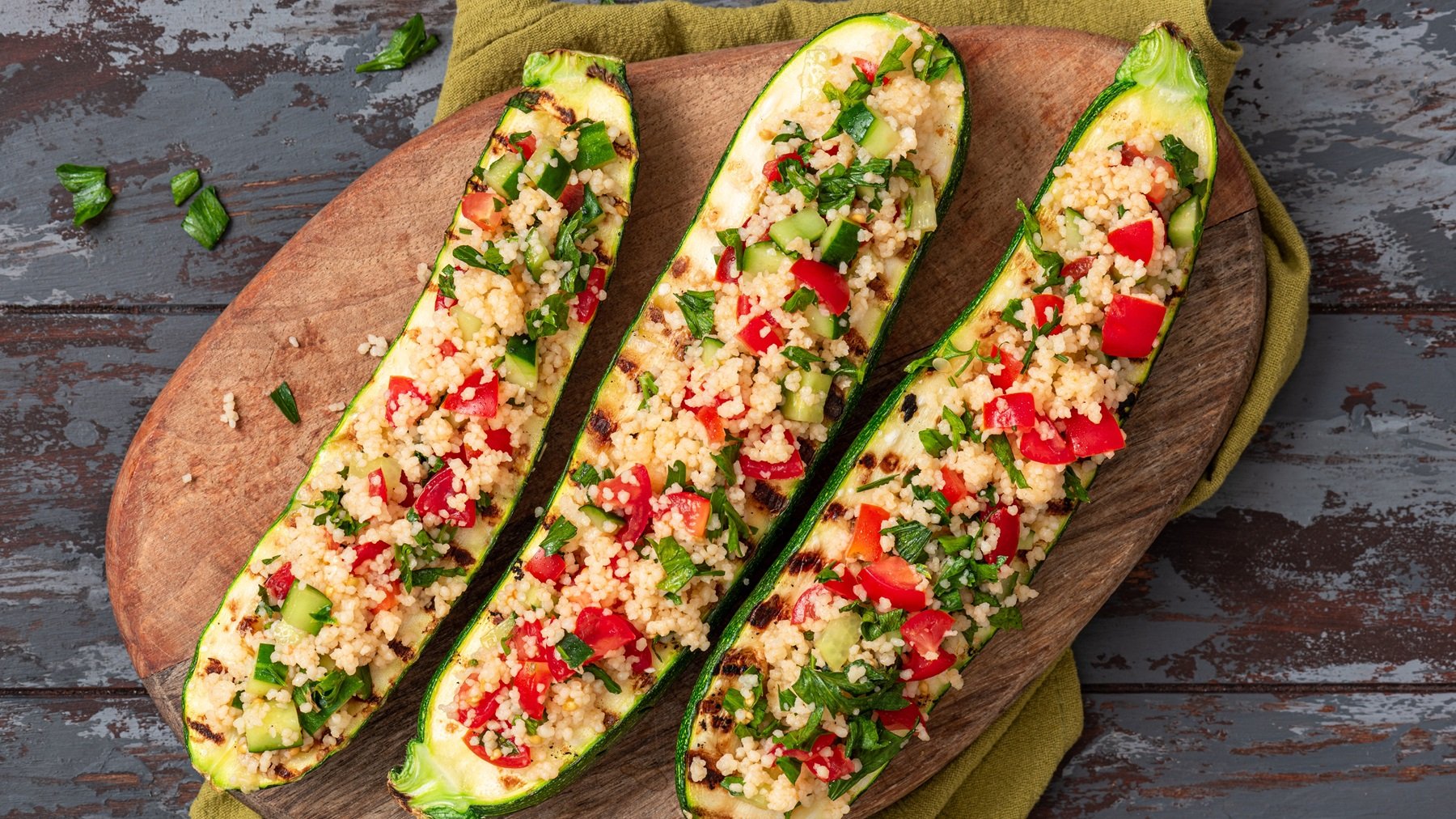 Drei gefüllte Zucchinihälften mit dem Couscous auf einem grauen Untergrund direkt von oben fotografiert.