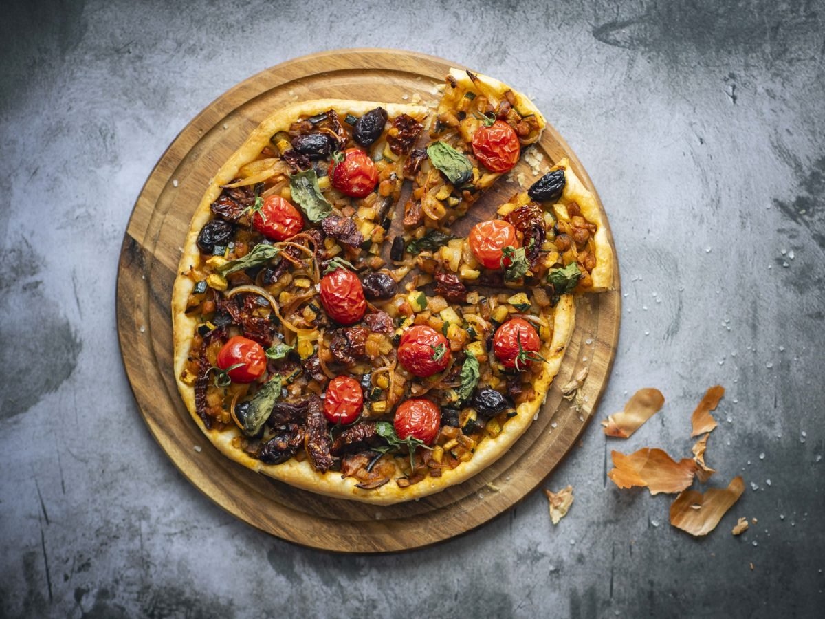 Die Gemüsepizza von oben auf einem Holzbrett und grauem Tisch fotografiert.