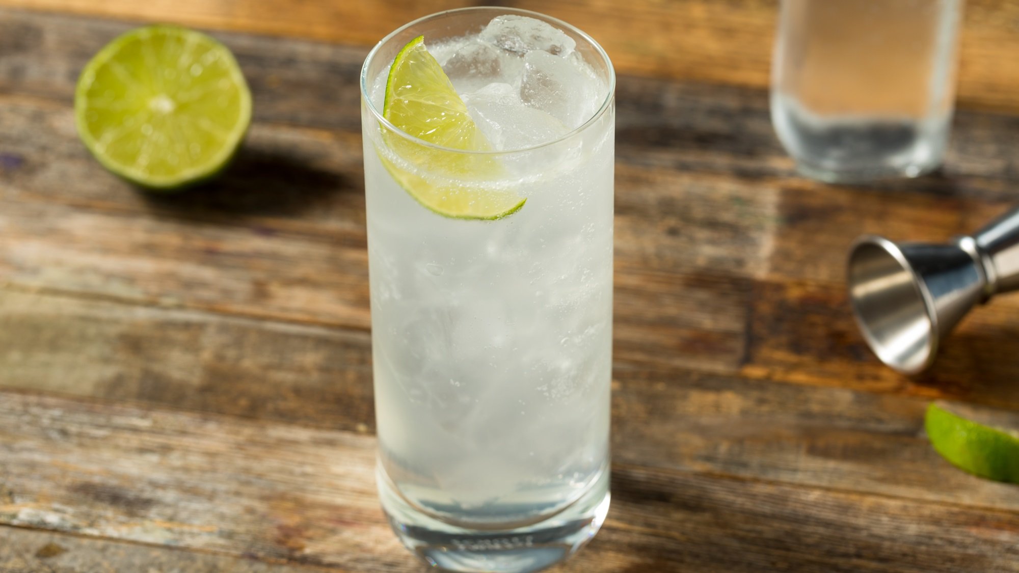 Erfrischender Ranch Water Cocktail mit Limettenscheibe und Eis in hohem Glas auf einem verwitterten Holztisch mit Barzubehör.