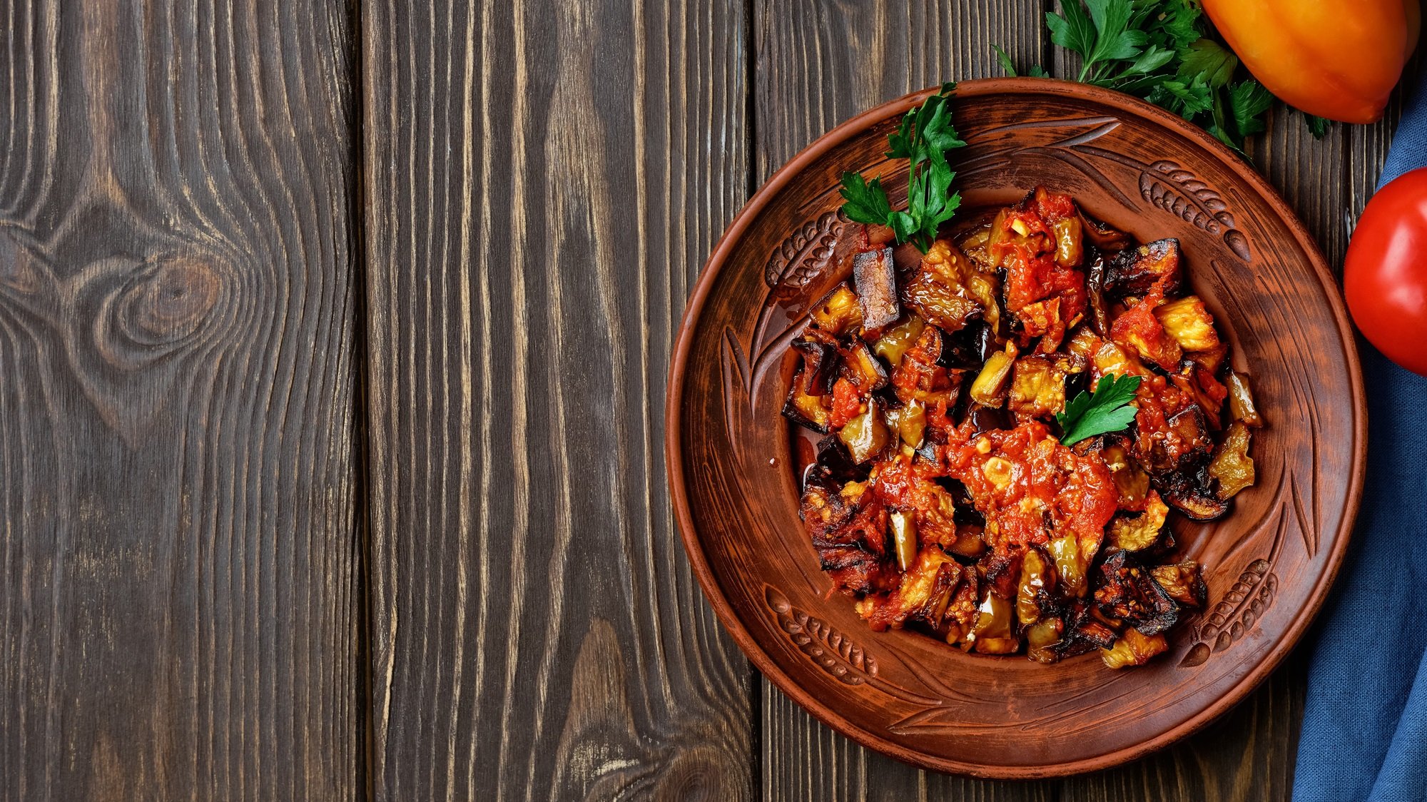 Traditionelle Şakşuka mit gebratenen Auberginen in Tomatensauce, angerichtet auf Keramikteller auf dunklem Holz.
