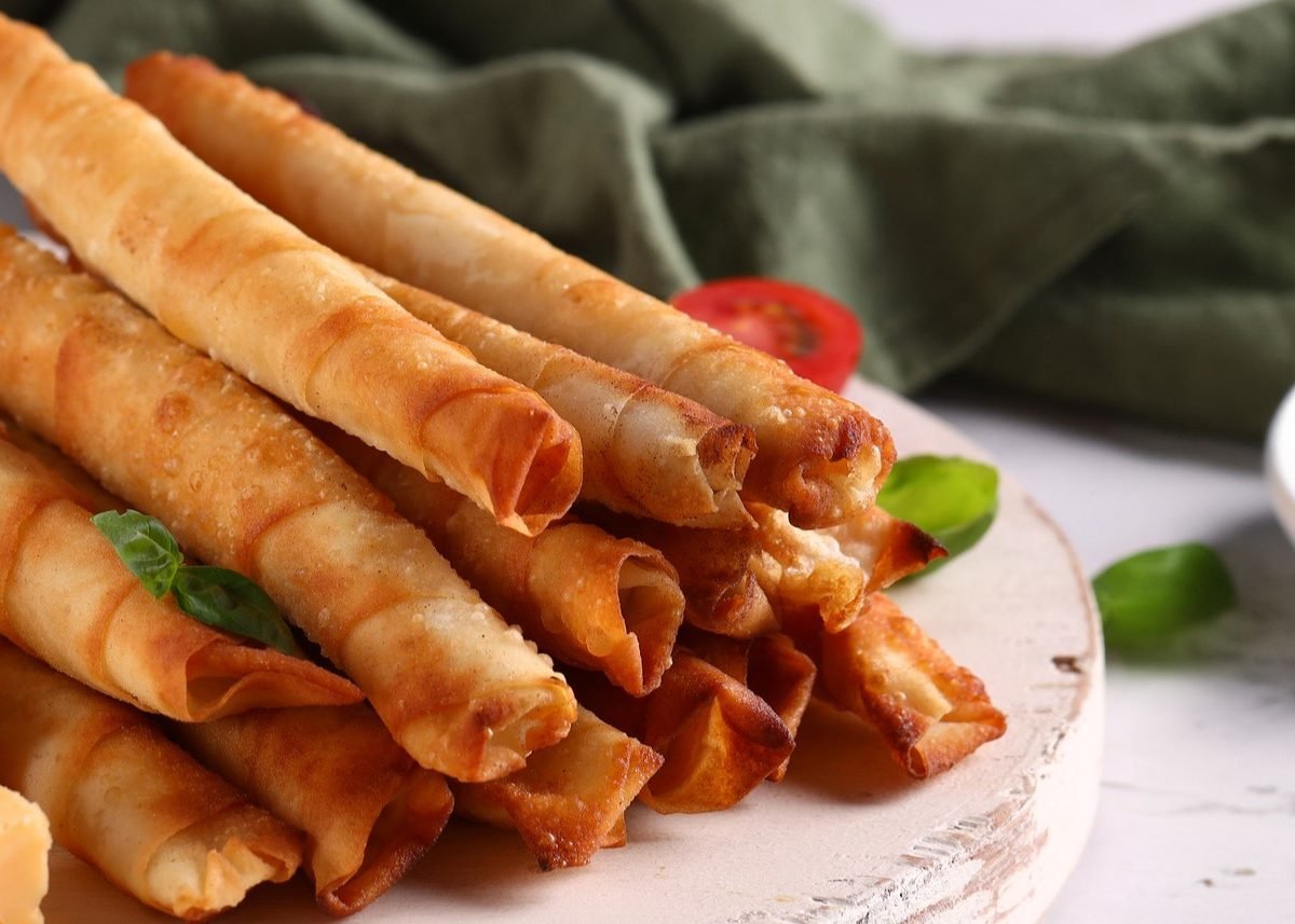 Mehrere Sigara Börek auf einem hellen Teller mit weißem Untergrund von der Seite fotografiert.