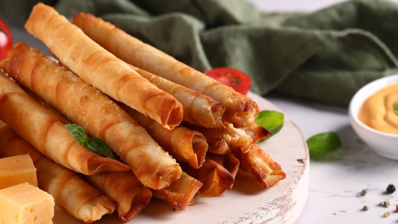 Mehrere Sigara Börek auf einem hellen Teller mit weißem Untergrund von der Seite fotografiert.