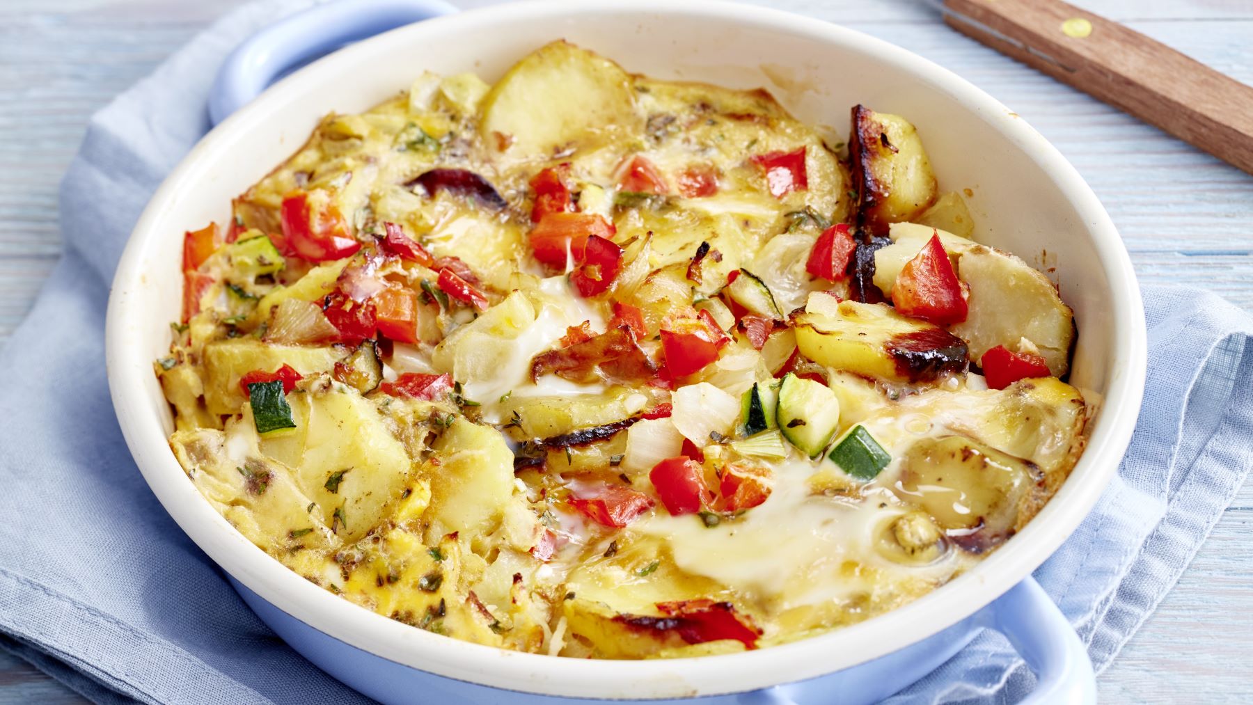 Bauernfrühstück mit Kartoffeln, Paprika und Zucchini in einer weißen Auflaufform – leichtes Gericht mit mediterranen Kräutern.