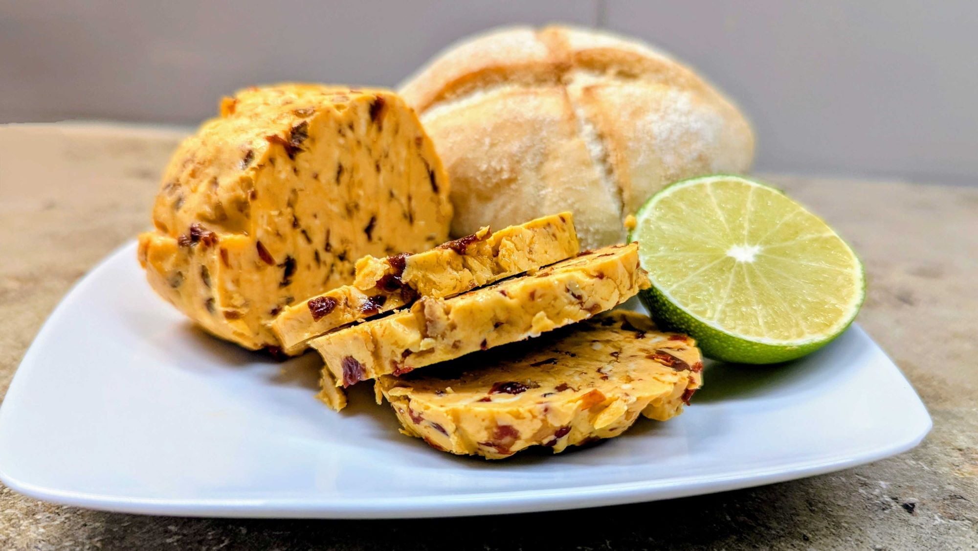Chili-Butter mit Chipotle in Scheiben geschnitten auf einem weißen Teller mit Brötchen und Limette im Hintergrund.