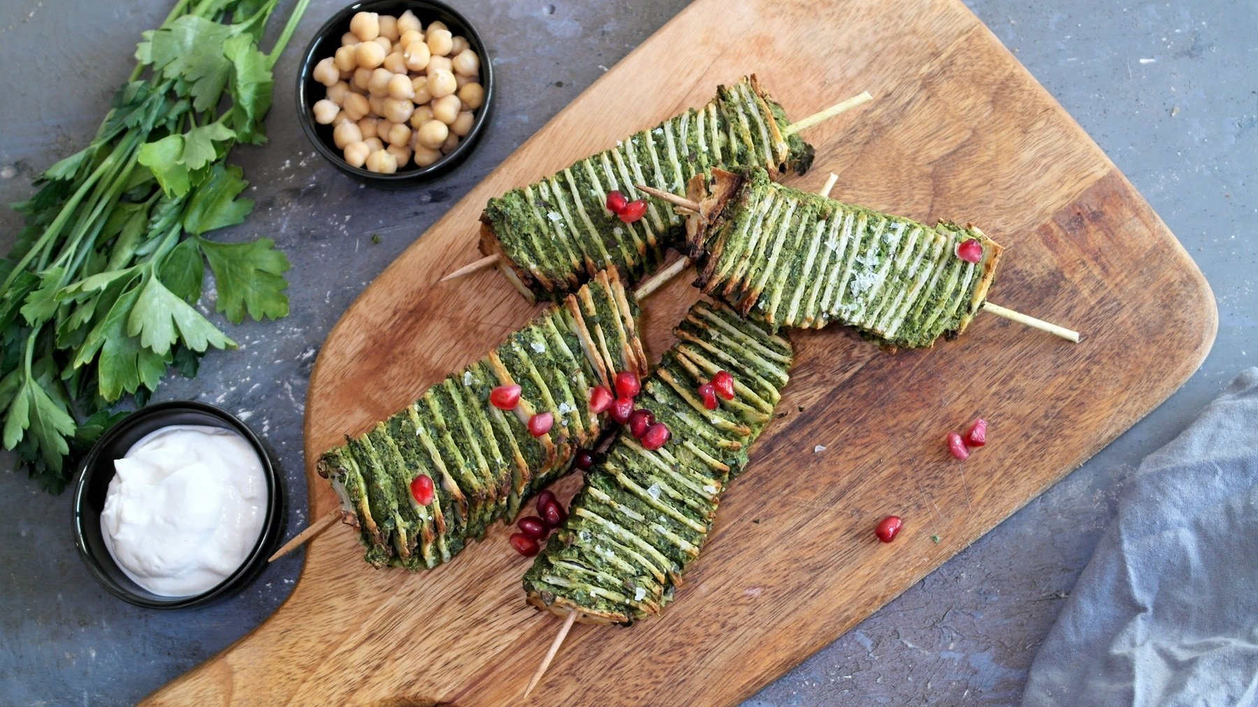 Mehrere Falafel-Spieße auf einem Holzbrett und grauem Steintisch direkt von oben fotografiert.