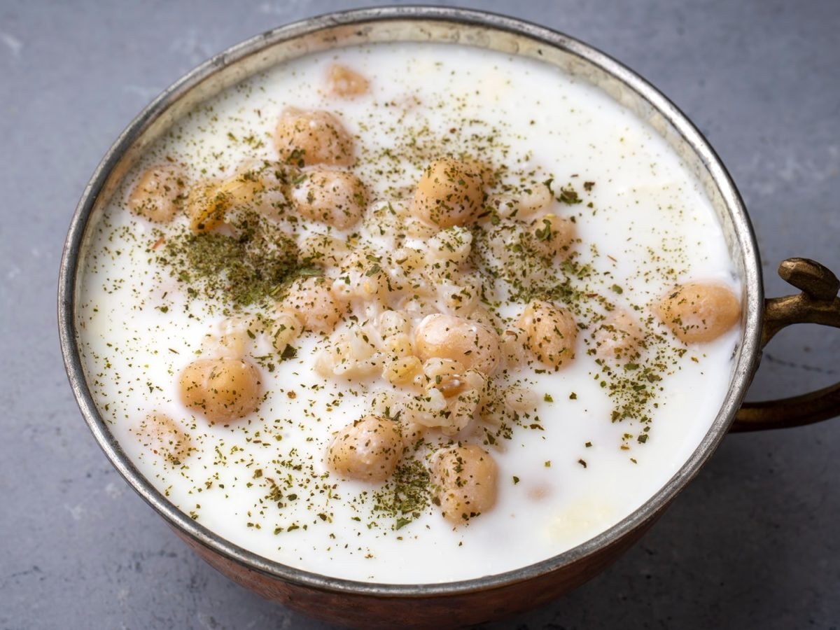 Cremige Joghurtsuppe mit Kichererbsen, Graupen und Minze in einer bronzefarbenen Schale auf grauem Steinuntergrund.