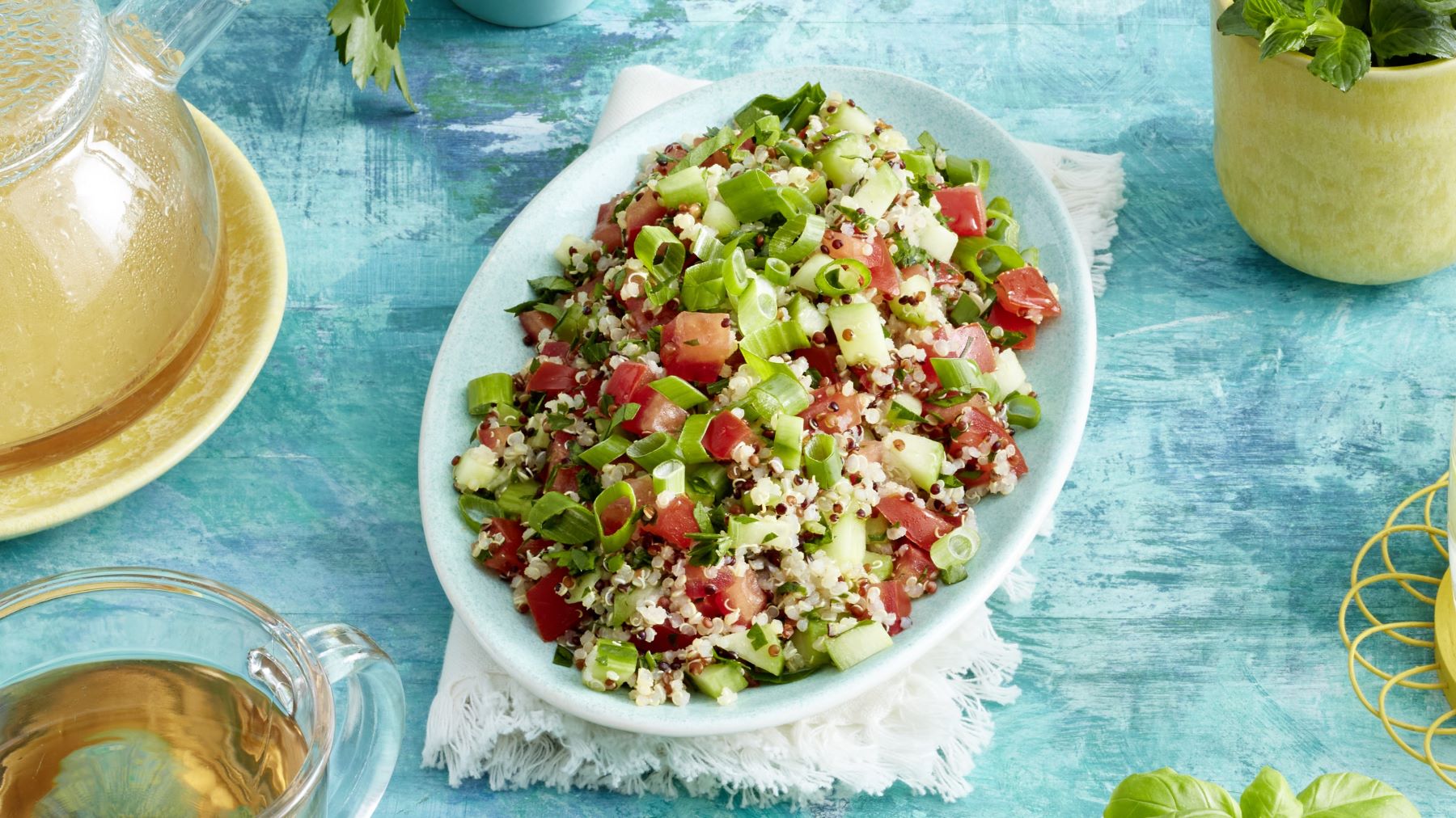 Frischer Petersiliensalat mit Quinoa, Tomaten, Gurken und Frühlingszwiebeln auf türkisfarbener Tischdecke angerichtet.